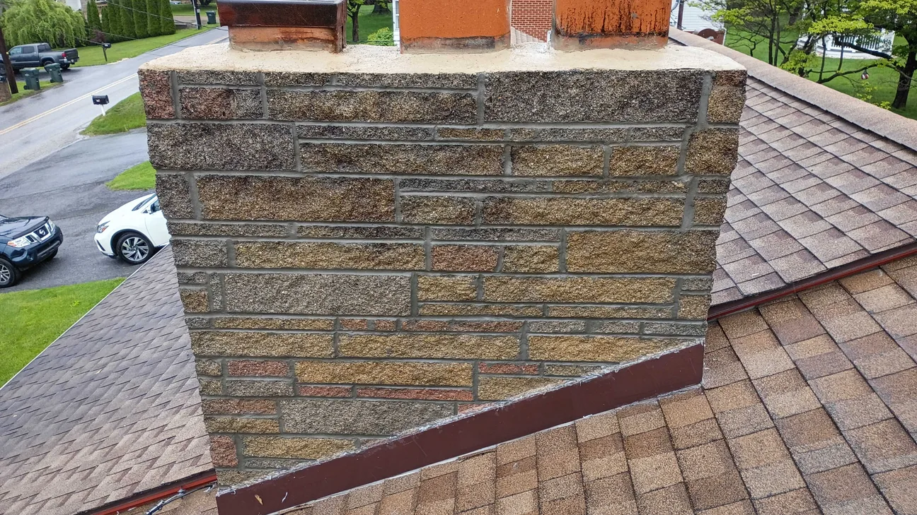 A stone veneer chimney with fresh mortar joints on a shingle roof, masonry contractor work