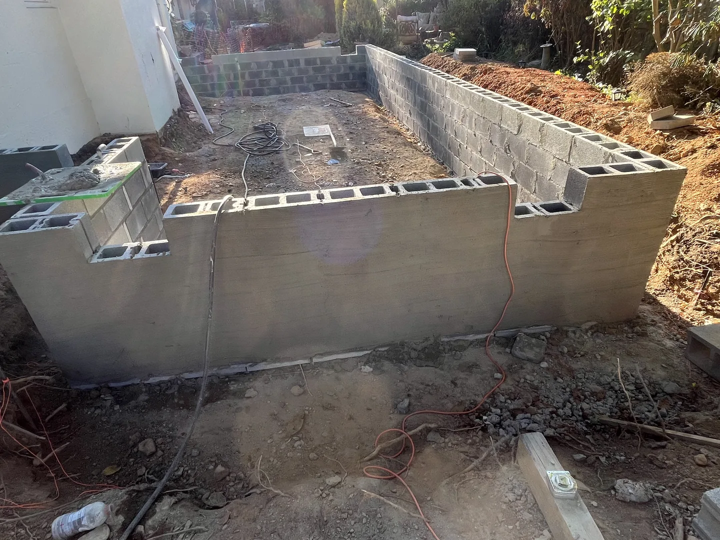 Concrete block foundation walls rising beside a house on a dirt site, block walls