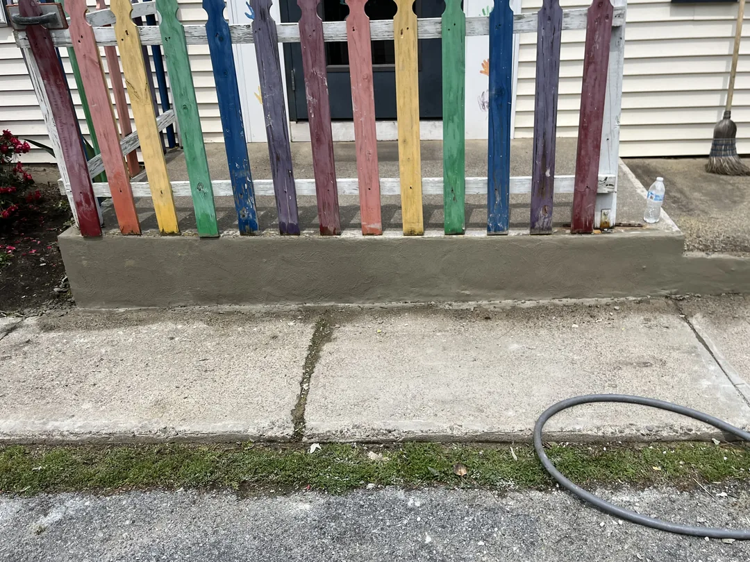 A freshly parged low wall under a picket fence beside a sidewalk, block walls