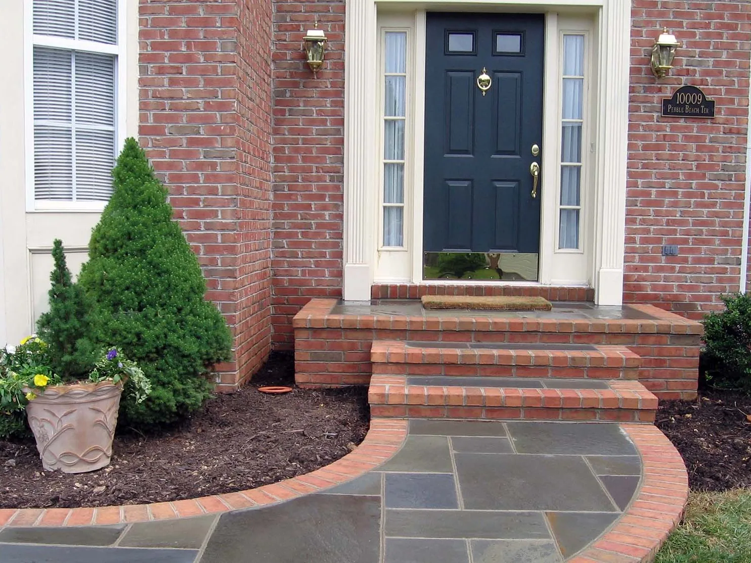 A brick front stoop and steps with stone treads at a brick house, brick masonry