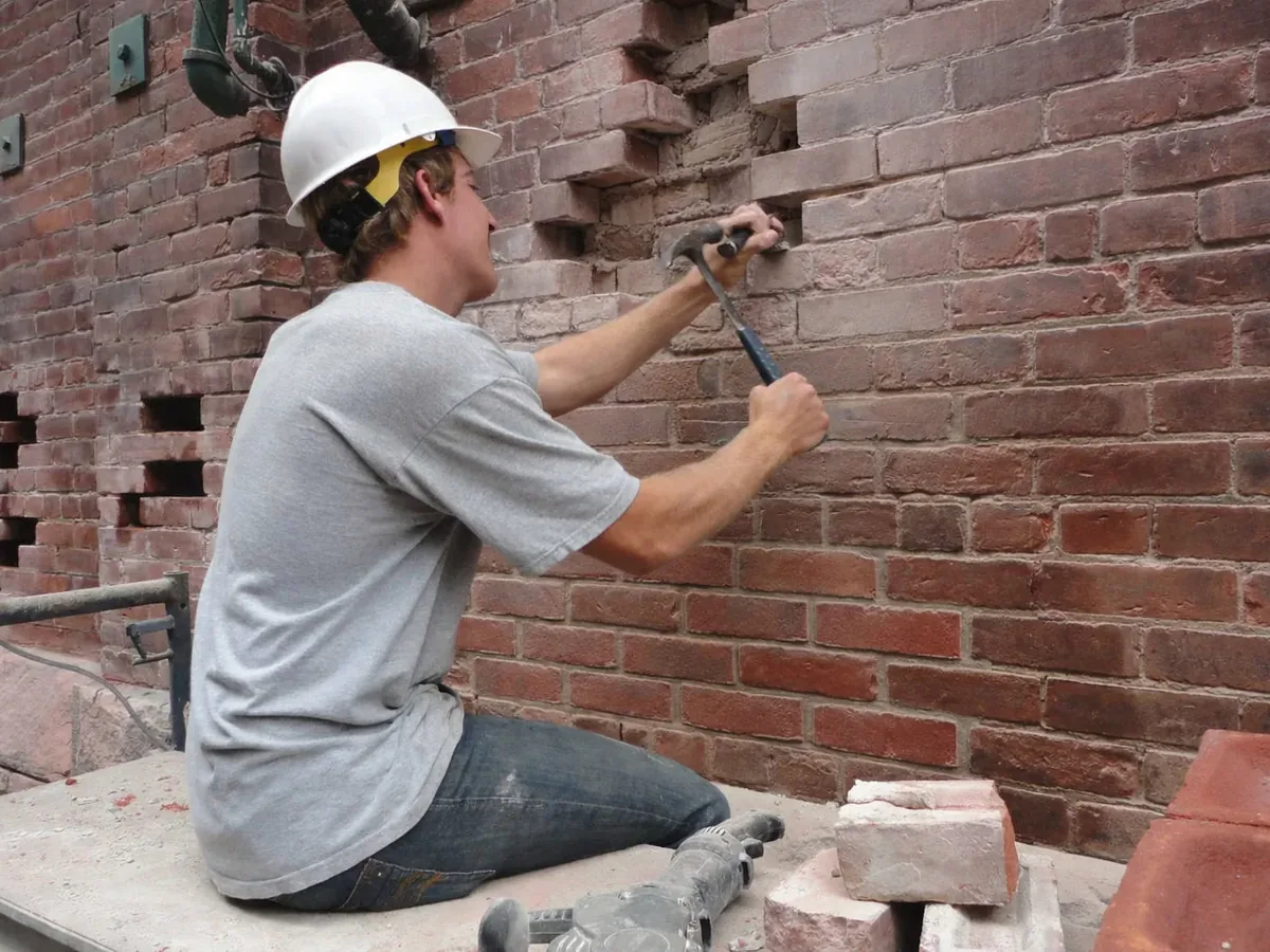 A mason cutting out damaged bricks from an old red brick wall, brick repair