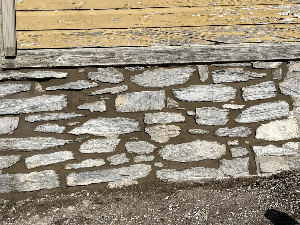 An old stone foundation wall with fresh mortar joints below wood siding, brick repair