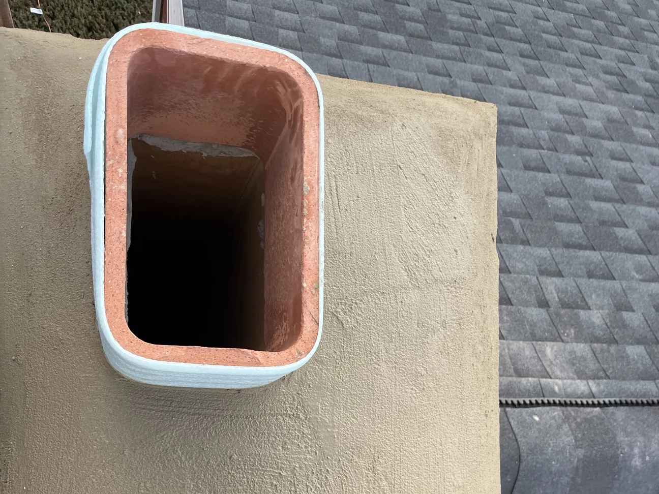 A new mortar chimney crown around clay flue tiles on a shingle roof, chimney repair