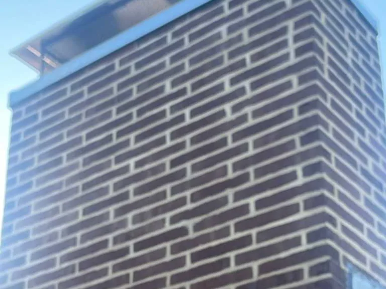 A dark brick chimney with fresh light mortar joints and a metal cap, chimney repair