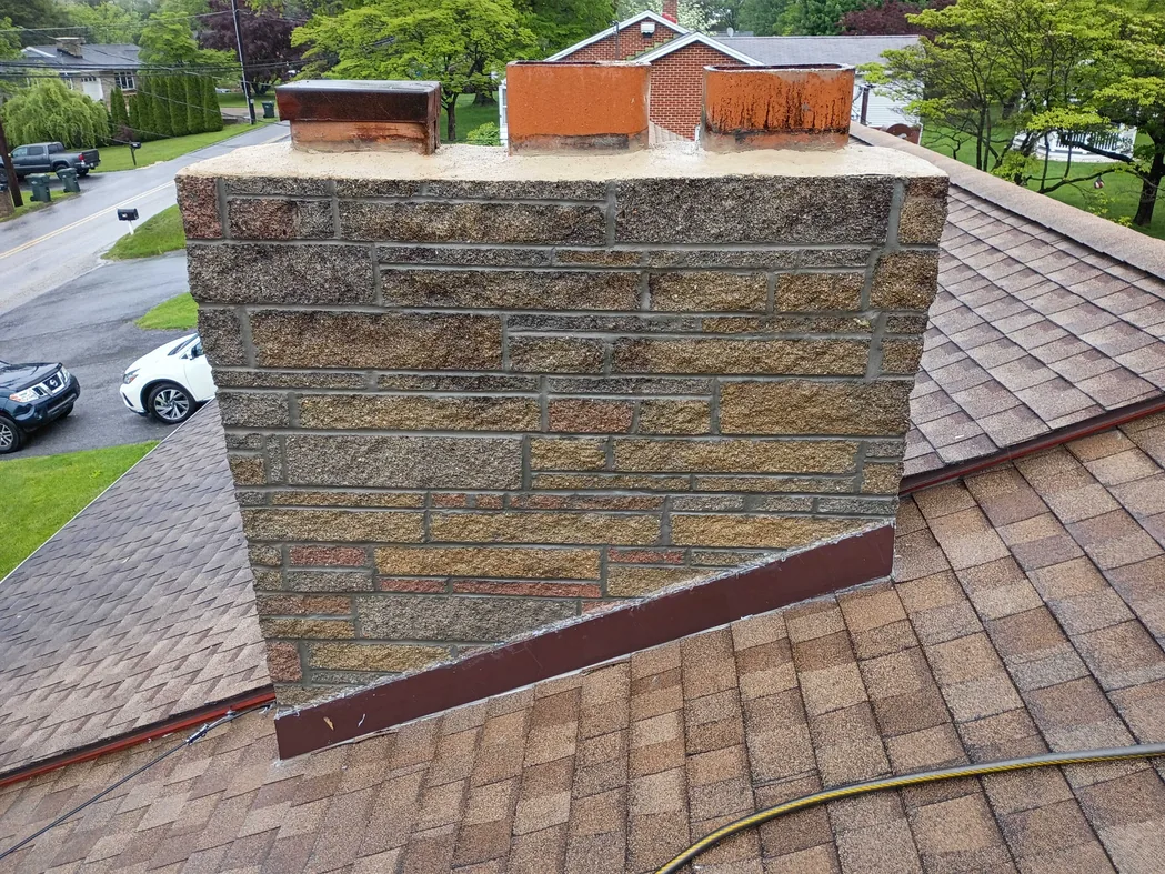 A stone veneer chimney with fresh mortar joints and clay flue tiles on a shingle roof, chimney repair