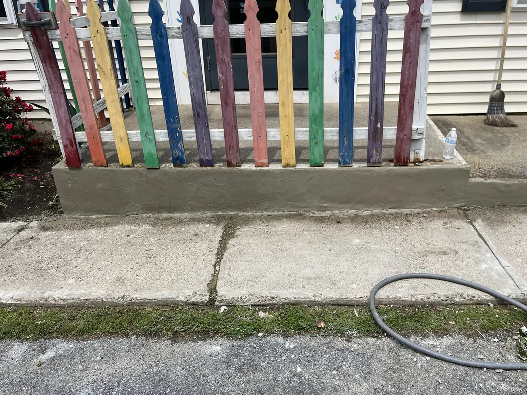 A freshly parged low wall under a picket fence beside a concrete sidewalk, concrete work