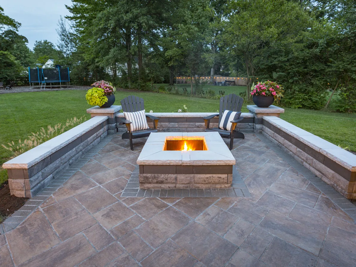 A square block fire pit with stone caps between low block seat walls on a paver patio, outdoor fireplaces and fire pits