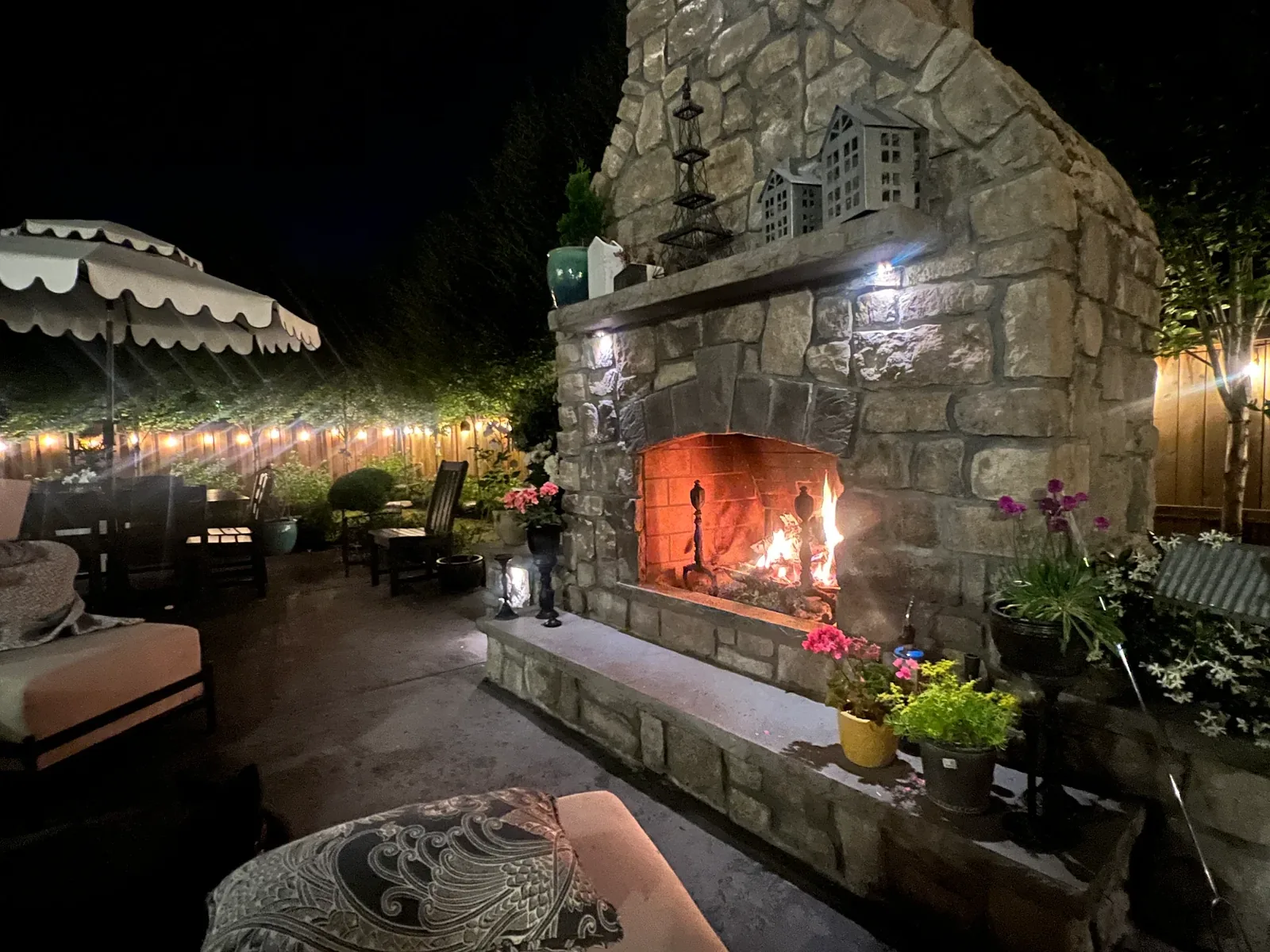 A natural stone outdoor fireplace with a fire burning and a raised stone hearth on a patio, outdoor fireplaces and fire pits