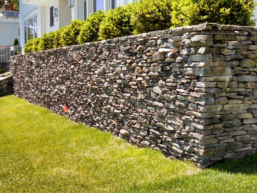 A long dry stacked natural stone retaining wall holding a raised shrub bed above a lawn, retaining walls