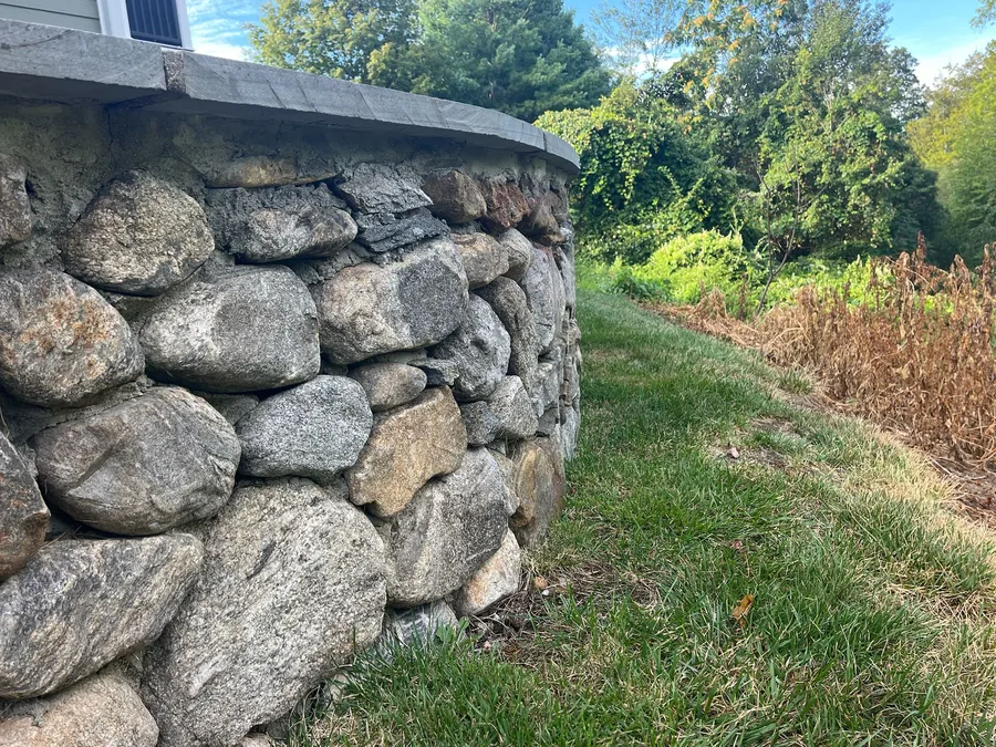 A curved mortared fieldstone retaining wall with a flat stone cap beside a lawn, retaining walls