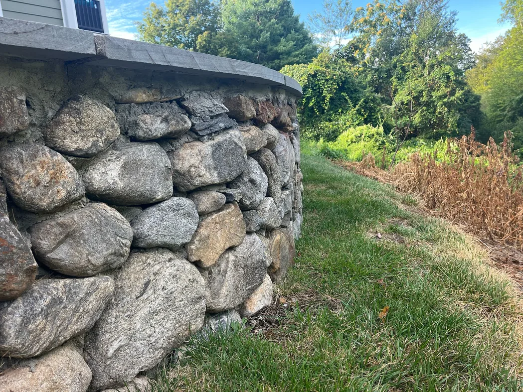A curved mortared fieldstone wall with a flat stone cap beside a lawn, stone masonry