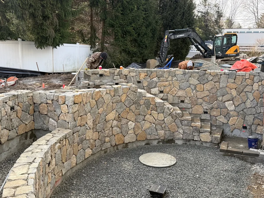 A curved mortared natural stone wall with built in steps under construction in a back yard, stone masonry