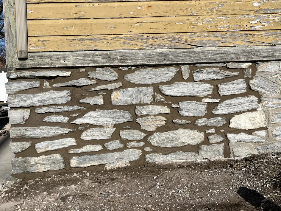 An old stone foundation wall with fresh mortar joints below wood siding, stone masonry
