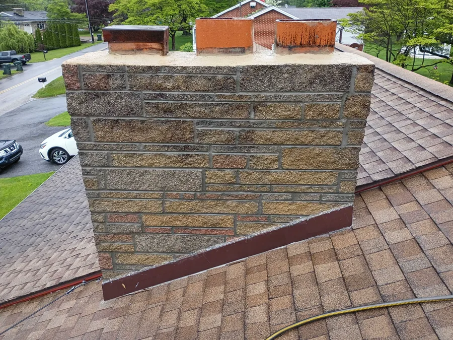 A stone veneer chimney with fresh mortar joints and clay flue tiles on a shingle roof, stone masonry