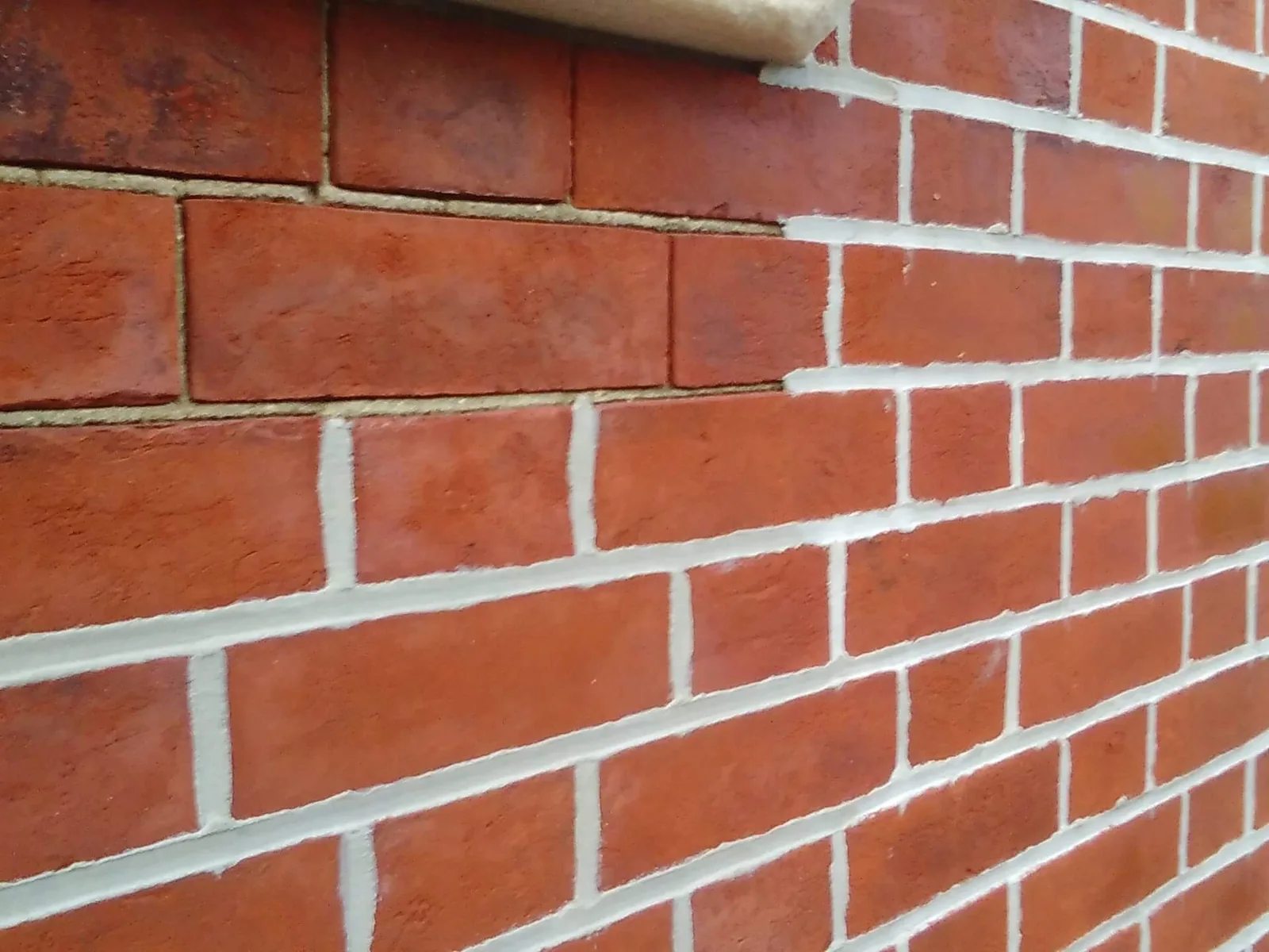 A red brick wall with fresh light mortar joints below old weathered joints, tuckpointing
