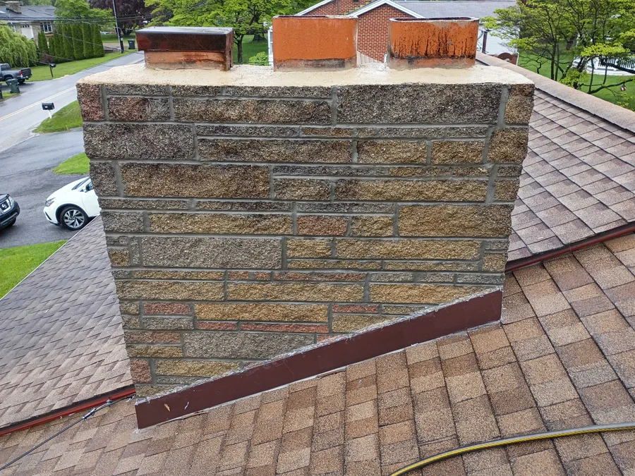 A stone veneer chimney with fresh mortar joints on a shingle roof, tuckpointing